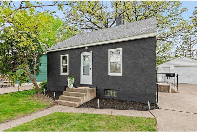 view of front of house featuring concrete driveway, an outdoor structure, a chimney, a shingled roof, and a detached garage