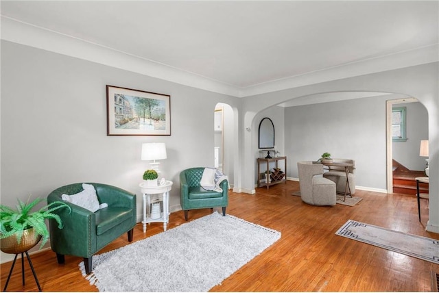 sitting room with arched walkways, wood finished floors, baseboards, and crown molding