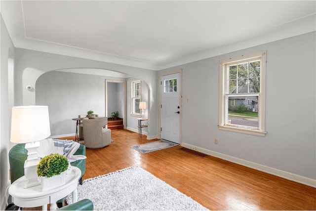 entryway featuring arched walkways, wood finished floors, and baseboards