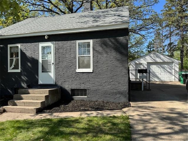 bungalow-style house featuring a garage, an outdoor structure, a chimney, roof with shingles, and driveway