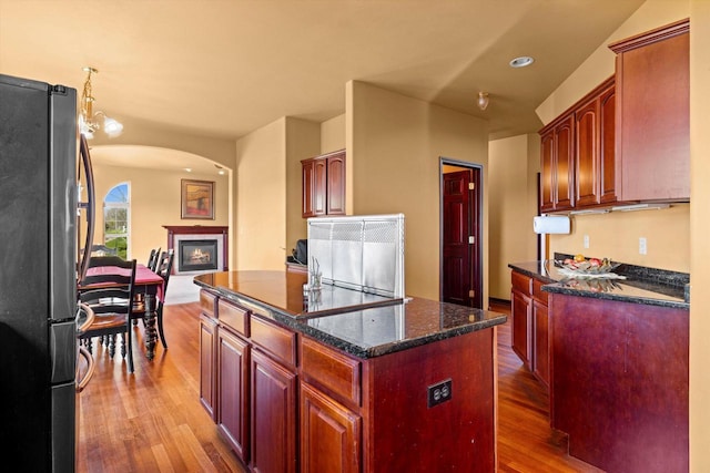 N109W14760 Preserve Pkwy, Germantown, WI 53022 - kitchen featuring freestanding refrigerator, wood finished floors, arched walkways, a glass covered fireplace, and dark stone countertops