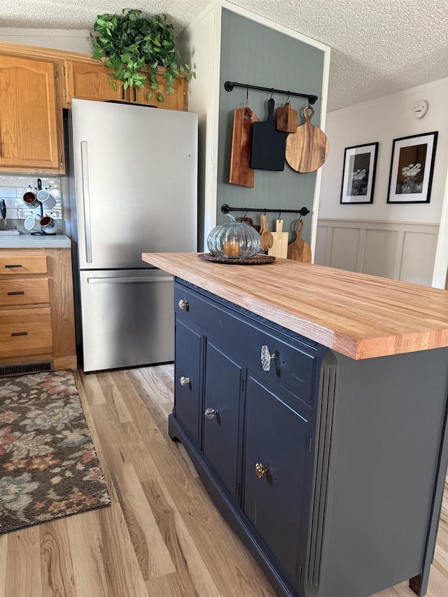 33150 Donna Dr Unit 14, Prairie Du Chien, WI 53821 - kitchen featuring freestanding refrigerator, a textured ceiling, blue cabinetry, light wood-style floors, and wooden counters