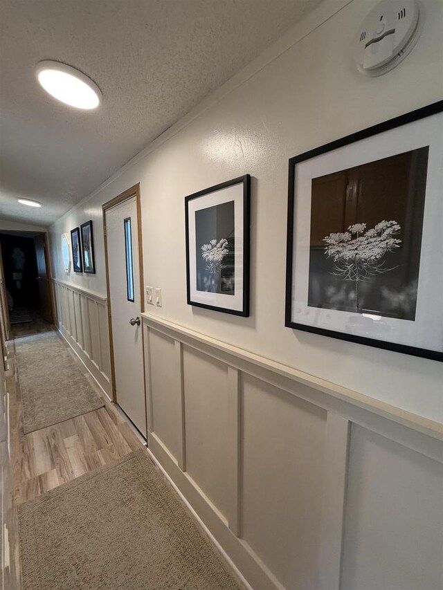 33150 Donna Dr Unit 14, Prairie Du Chien, WI 53821 - corridor featuring a textured ceiling, a wainscoted wall, light wood finished floors, and a decorative wall