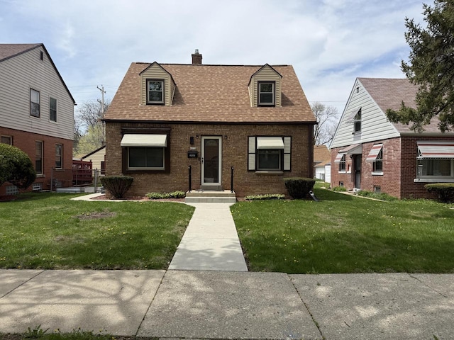 view of front facade with a chimney, a front yard, brick siding, and a shingled roof