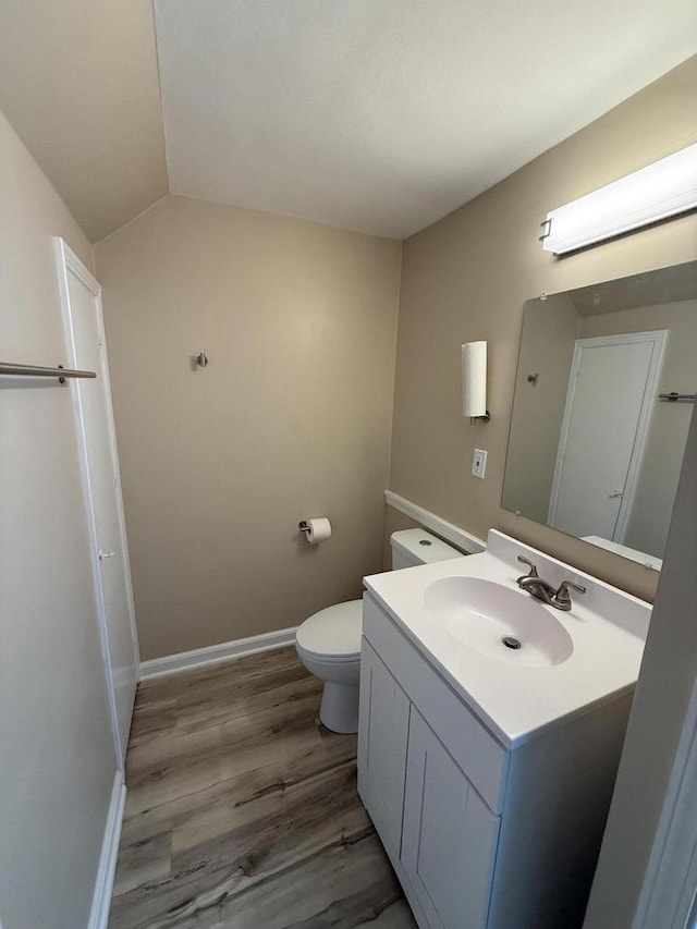 bathroom with vanity, wood finished floors, toilet, vaulted ceiling, and baseboards