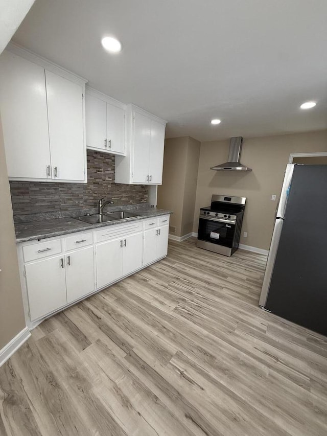 kitchen with stainless steel appliances, wall chimney range hood, a sink, baseboards, and light wood-type flooring