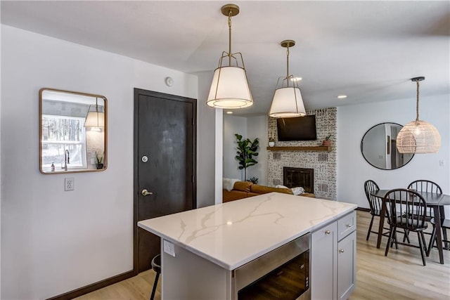 E1924 Kirk Ct, Eau Claire, WI 54701 - kitchen featuring light wood finished floors, a brick fireplace, a center island, pendant lighting, and light stone counters