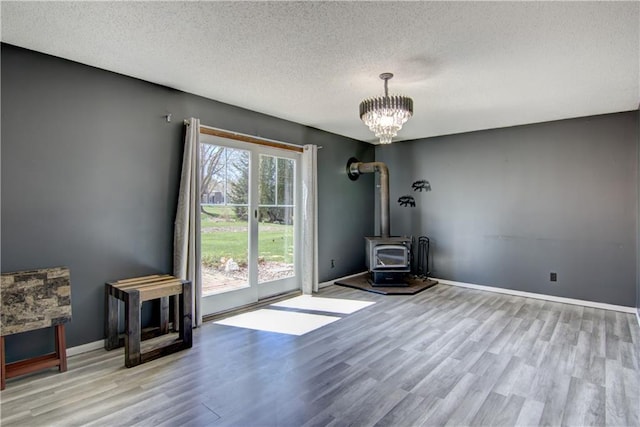 303 W Maple St, Thorp, WI 54771 - unfurnished dining area featuring wood finished floors, a textured ceiling, a wood stove, a chandelier, and baseboards