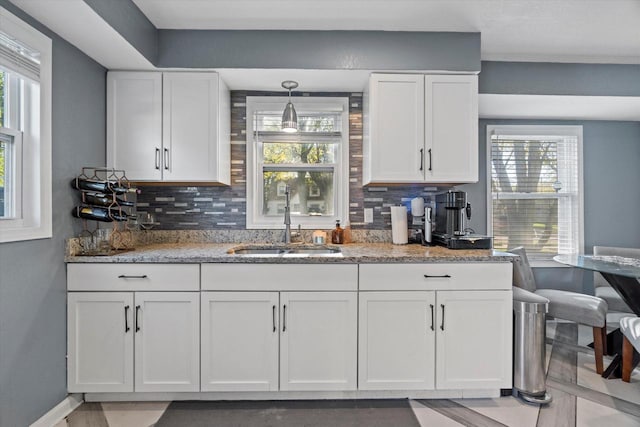 kitchen featuring a sink, white cabinetry, light stone countertops, tasteful backsplash, and baseboards