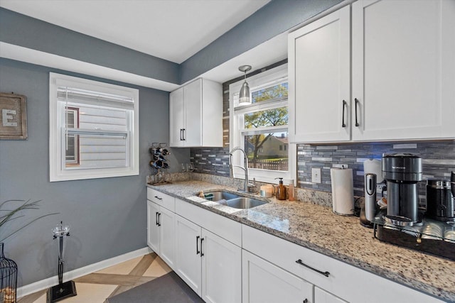 kitchen with a sink, tasteful backsplash, white cabinetry, and baseboards