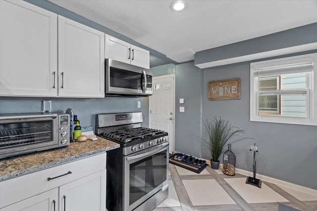 kitchen with stainless steel appliances, light stone countertops, white cabinets, and baseboards