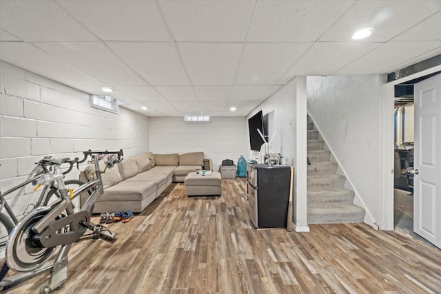 living room with wood finished floors, stairs, a drop ceiling, recessed lighting, and concrete block wall
