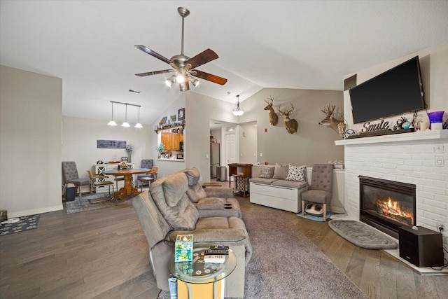 living area with wood finished floors, a ceiling fan, vaulted ceiling, and a brick fireplace