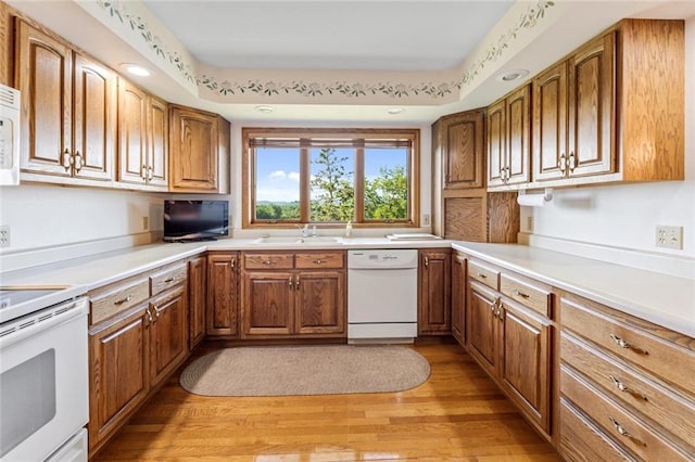 kitchen featuring white appliances, a sink, light wood finished floors, brown cabinets, and light countertops