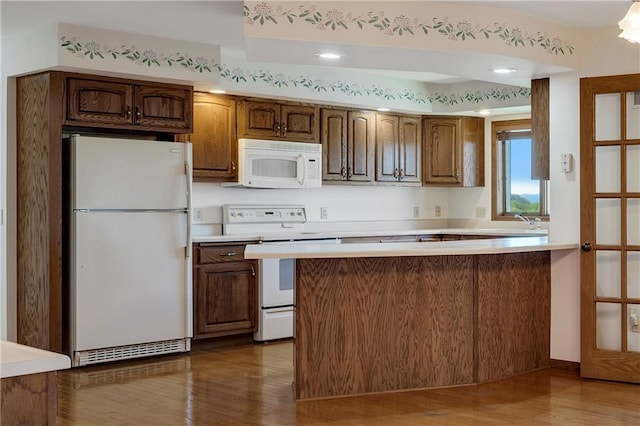 kitchen with white appliances, wood finished floors, light countertops, and a peninsula