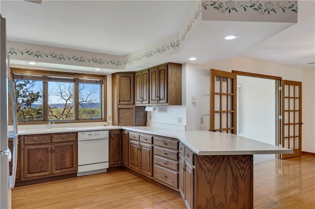 kitchen featuring dishwasher, a peninsula, light wood-style floors, a sink, and light countertops