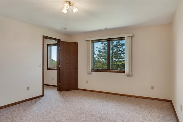 spare room featuring light carpet and baseboards