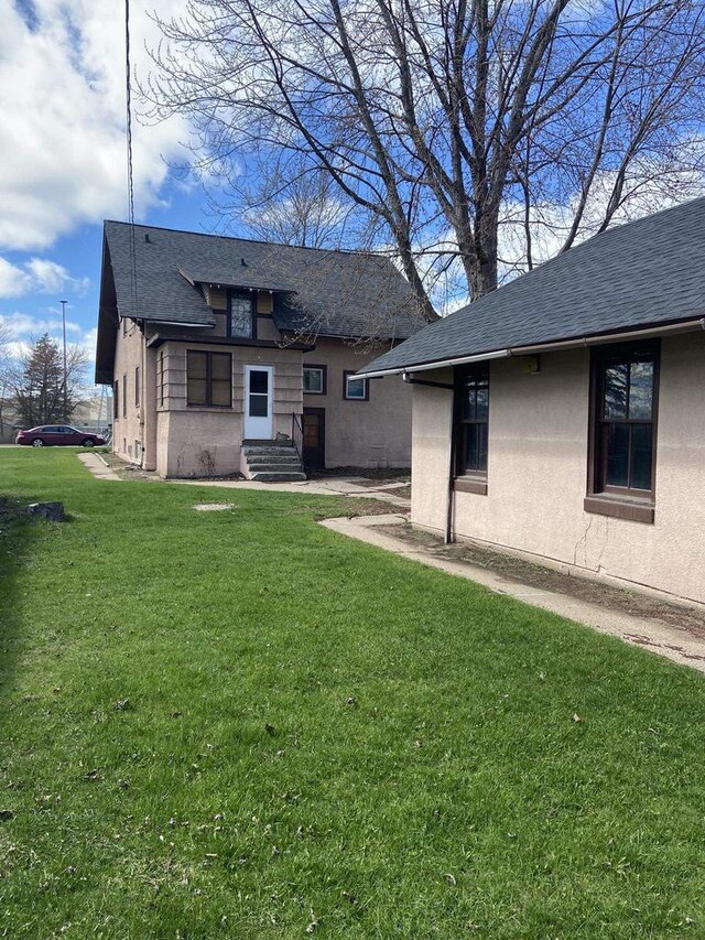 1040 N 1st St, Wisconsin Rapids, WI 54494 - back of house featuring a shingled roof, a yard, and stucco siding