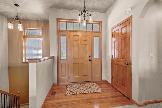 entryway with a chandelier, light wood-type flooring, arched walkways, and baseboards