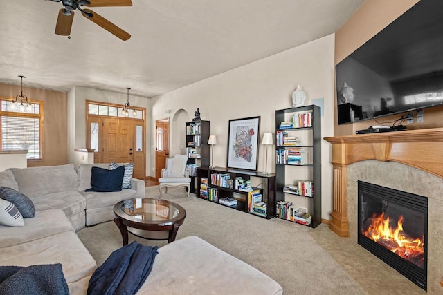 living area with a tile fireplace, carpet flooring, a ceiling fan, and arched walkways