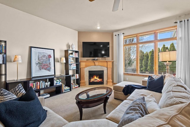 carpeted living area with a lit fireplace and a ceiling fan