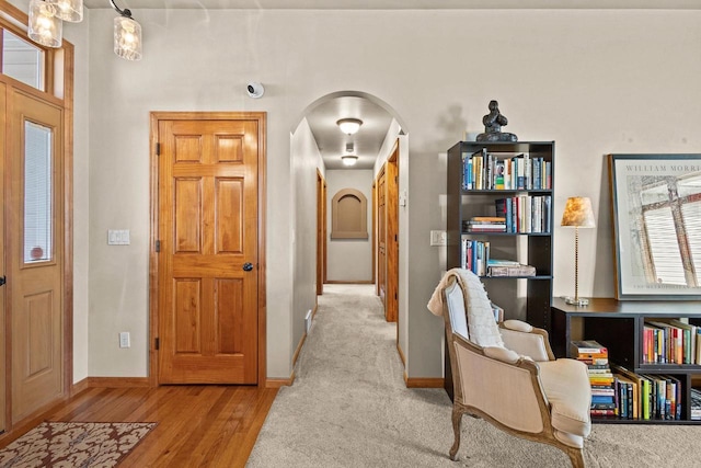hallway with arched walkways, baseboards, and wood finished floors