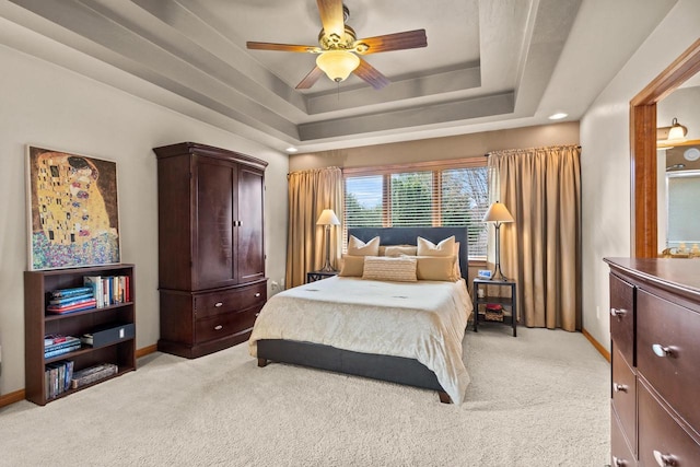 bedroom with light carpet, baseboards, a tray ceiling, and a ceiling fan