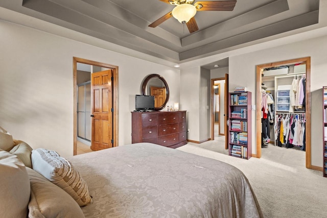 carpeted bedroom with a raised ceiling, a spacious closet, baseboards, a closet, and ceiling fan