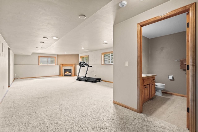 exercise area featuring a warm lit fireplace, baseboards, and light colored carpet