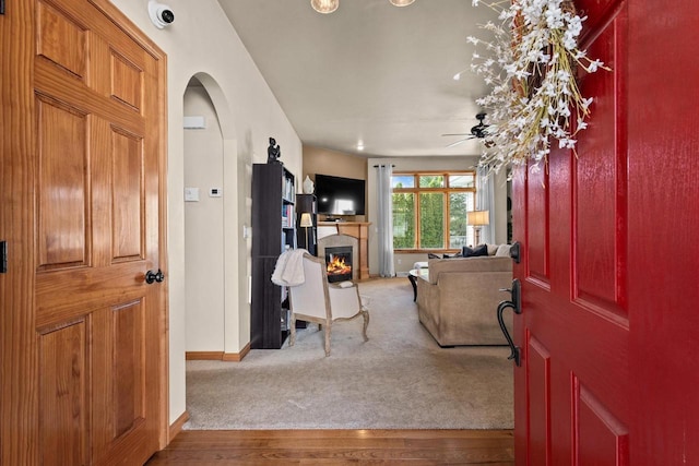 foyer entrance with arched walkways, a glass covered fireplace, baseboards, wood finished floors, and ceiling fan