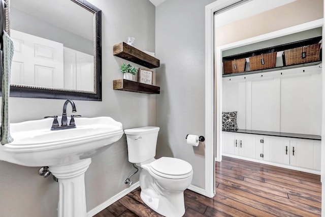half bath with toilet, wood finished floors, and baseboards