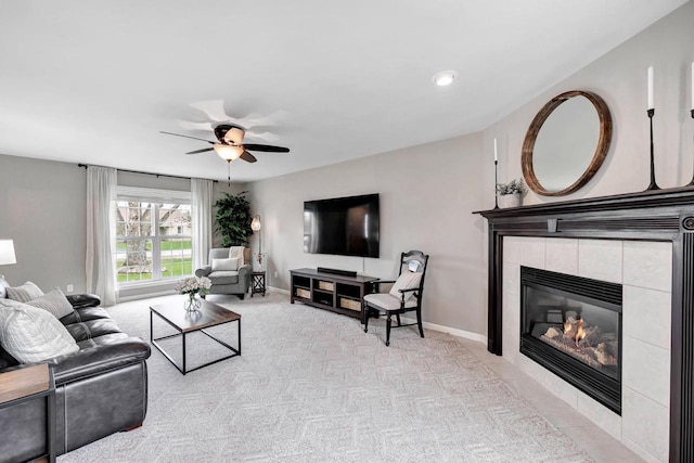 carpeted living room featuring a ceiling fan, a tile fireplace, and baseboards