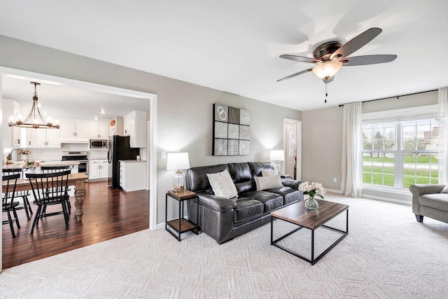 living area featuring dark colored carpet, ceiling fan, a chandelier, and baseboards