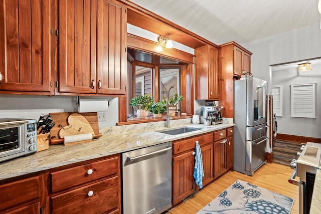 1753 Oneida Ct, Grafton, WI 53024 - kitchen featuring stainless steel appliances, a sink, light wood-style floors, light stone counters, and brown cabinets