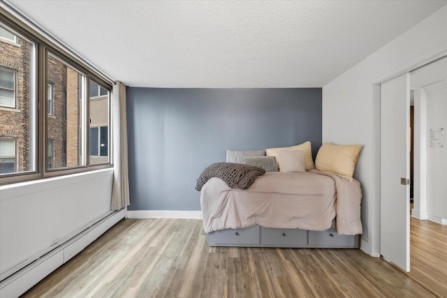 bedroom featuring baseboard heating, wood finished floors, baseboards, and a textured ceiling