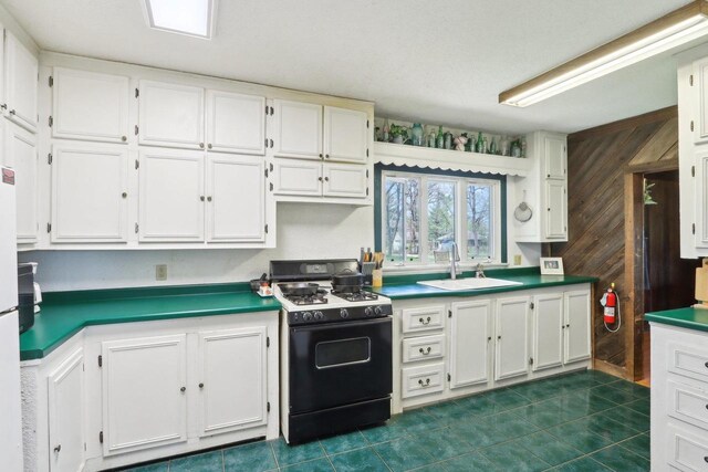 4121 1st Ave, Briggsville, WI 53920 - kitchen featuring gas range oven, a sink, white cabinetry, dark tile patterned floors, and wooden walls