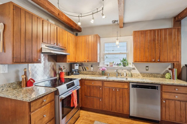 kitchen with appliances with stainless steel finishes, under cabinet range hood, a sink, light wood-style floors, and brown cabinetry