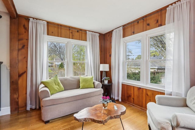 living area featuring baseboards, light wood finished floors, and wooden walls