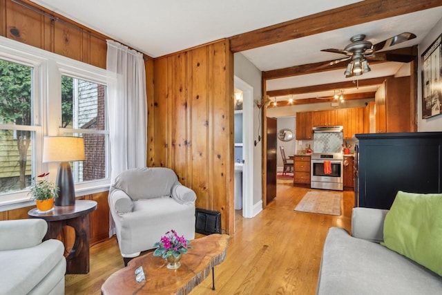living room featuring light wood-style floors, beam ceiling, ceiling fan, and wooden walls