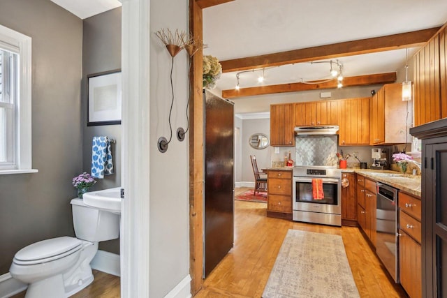 kitchen with stainless steel appliances, light wood-type flooring, brown cabinetry, under cabinet range hood, and tasteful backsplash