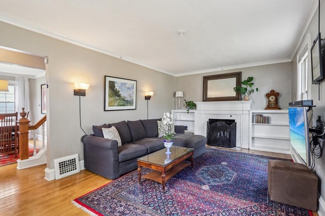living area with ornamental molding, wood finished floors, a brick fireplace, and baseboards