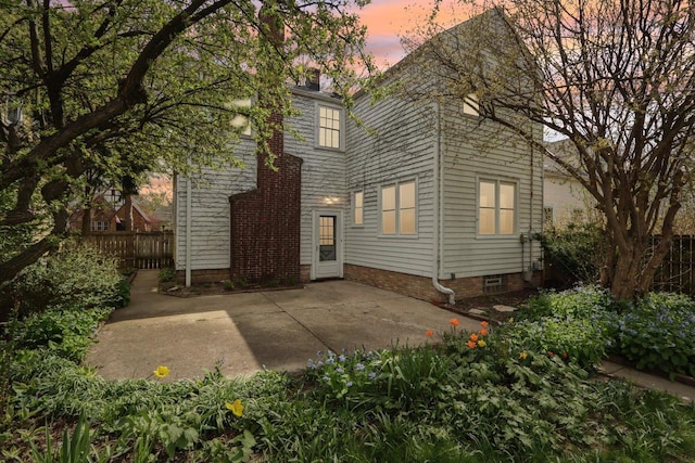back of house at dusk featuring a patio area, fence, and a chimney