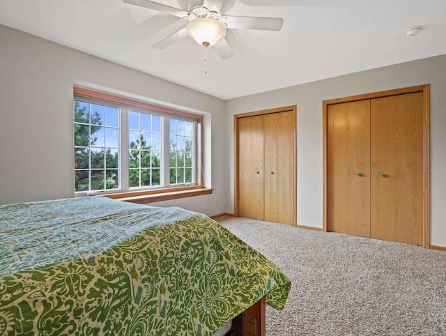 carpeted bedroom featuring two closets, baseboards, and a ceiling fan