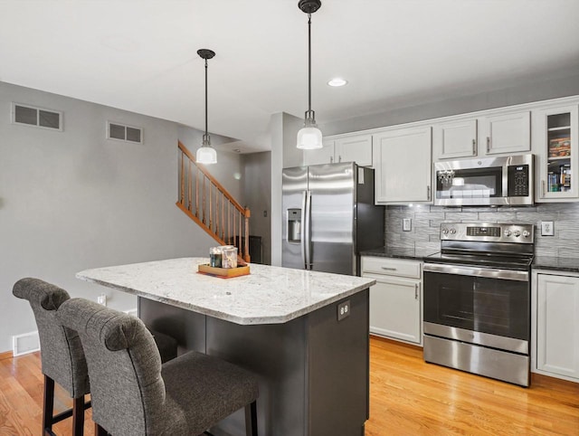 kitchen with stainless steel appliances, a center island, backsplash, light wood-type flooring, and a breakfast bar