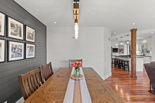 dining room with decorative columns, wood finished floors, wood walls, baseboards, and recessed lighting