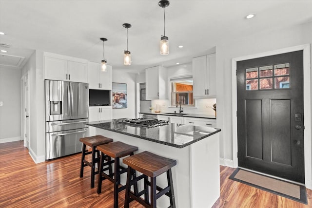 kitchen featuring stainless steel appliances, a sink, a center island, wood finished floors, and white cabinetry
