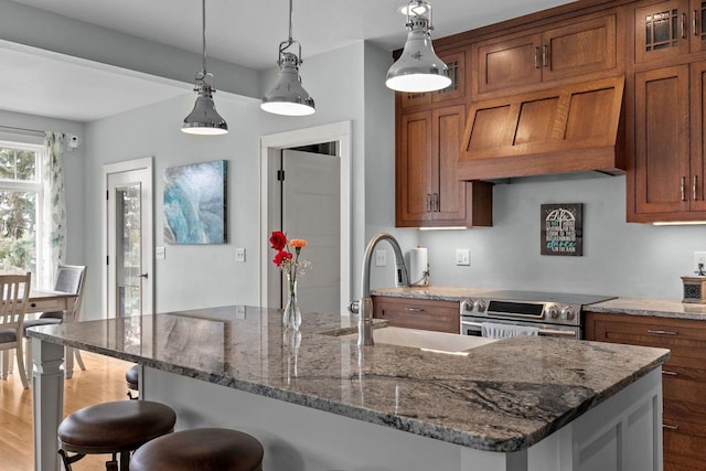 519 Park Ave, Little Chute, WI 54140 - kitchen featuring stainless steel range with electric stovetop, brown cabinetry, a sink, and a breakfast bar area