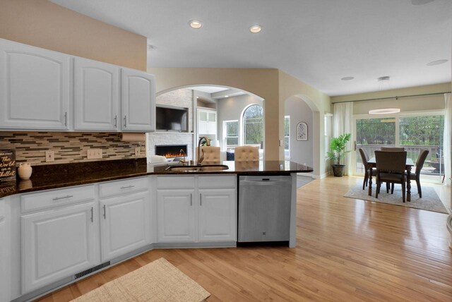 N53W16789 Prairie Dawn, Menomonee Falls, WI 53051 - kitchen featuring stainless steel dishwasher, a sink, a lit fireplace, light wood-style flooring, and decorative backsplash