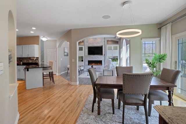N53W16789 Prairie Dawn, Menomonee Falls, WI 53051 - dining space with a fireplace, light wood finished floors, baseboards, recessed lighting, and arched walkways