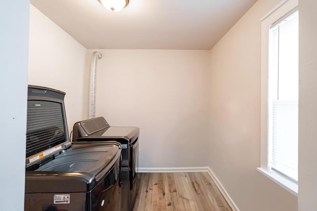 clothes washing area with washing machine and dryer, light wood-style floors, and baseboards